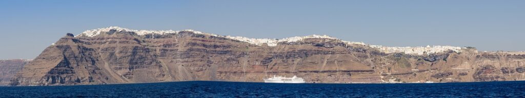 Fira along the caldera rim seen from the sea, with a cruise ship at anchor